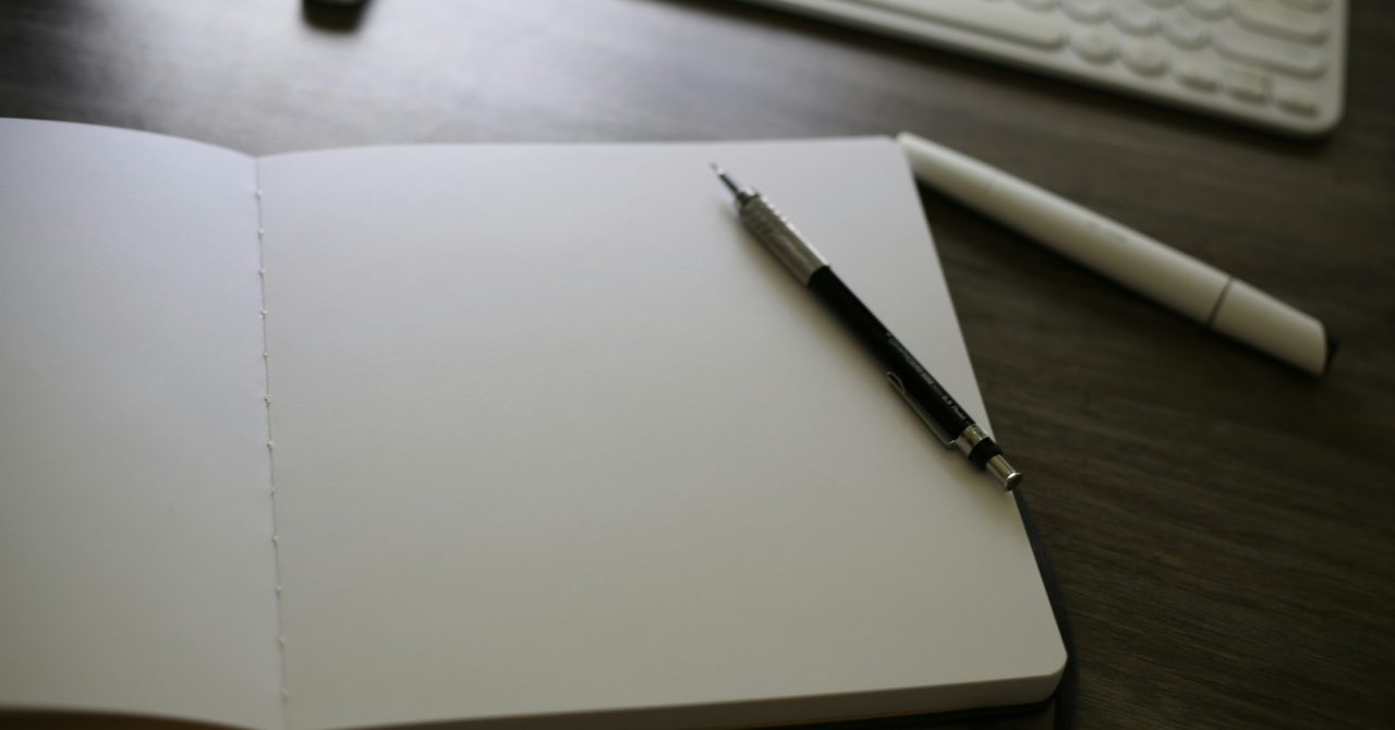 パソコンの前に開いたノートを置き、まず何を始めるか考える仕事机の実写写真